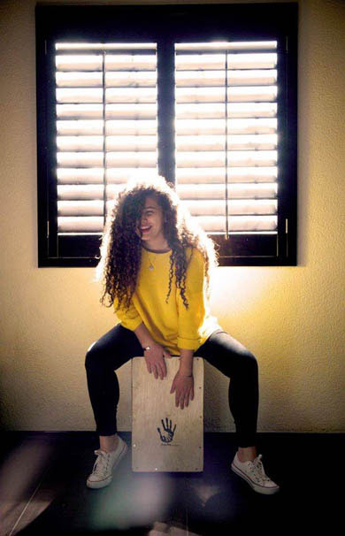 A woman plays a Drum Box Percussion cajon beneath a sun-filled window in Mexico.